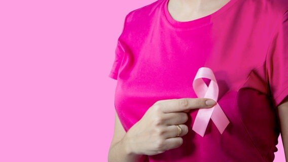 Frau im pinkfarbenen Shirt hält eine rosa Schleife vor die Brust (Symbolbild Brustkrebs). © Colourbox Foto: -
